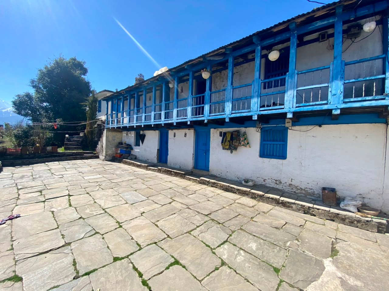 Traditional blue-balcony village house with a stone courtyard in Garhwal