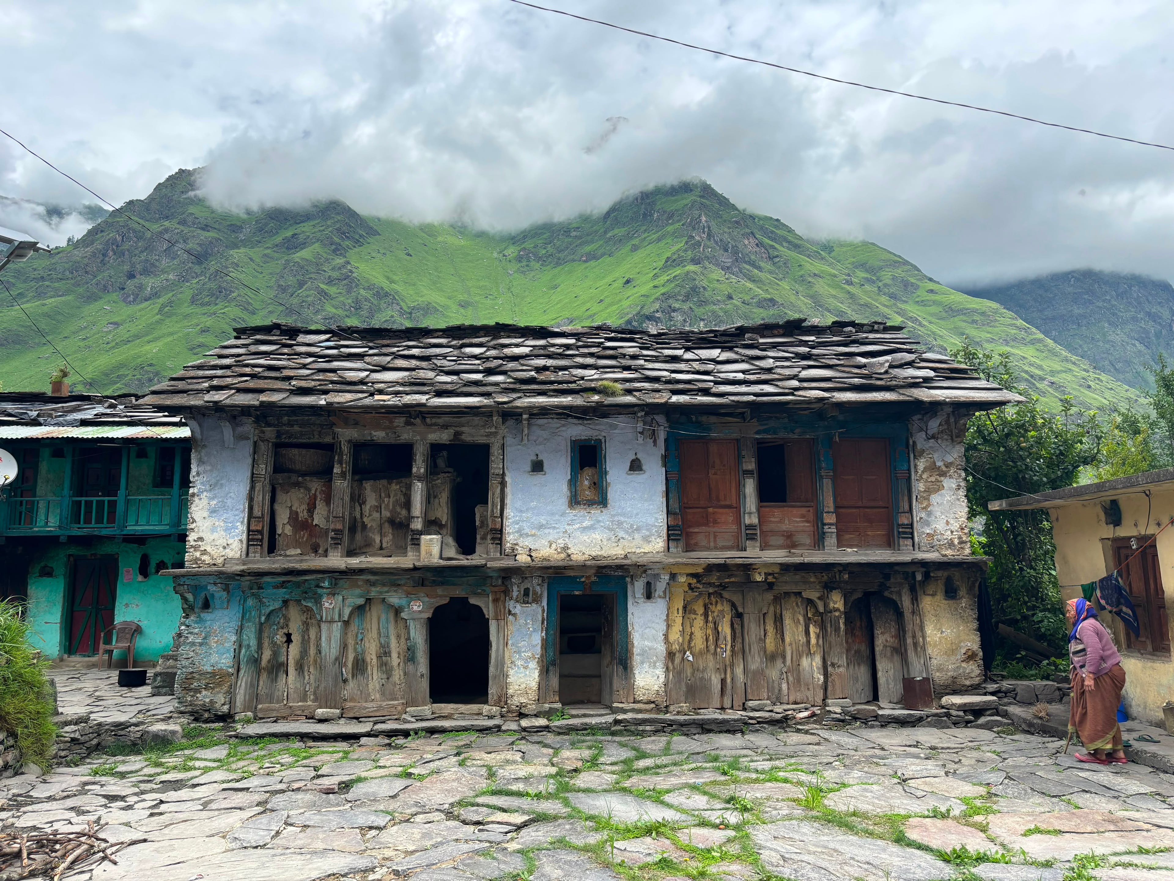 Old stone-roofed Garhwali house beneath cloud-covered green mountains